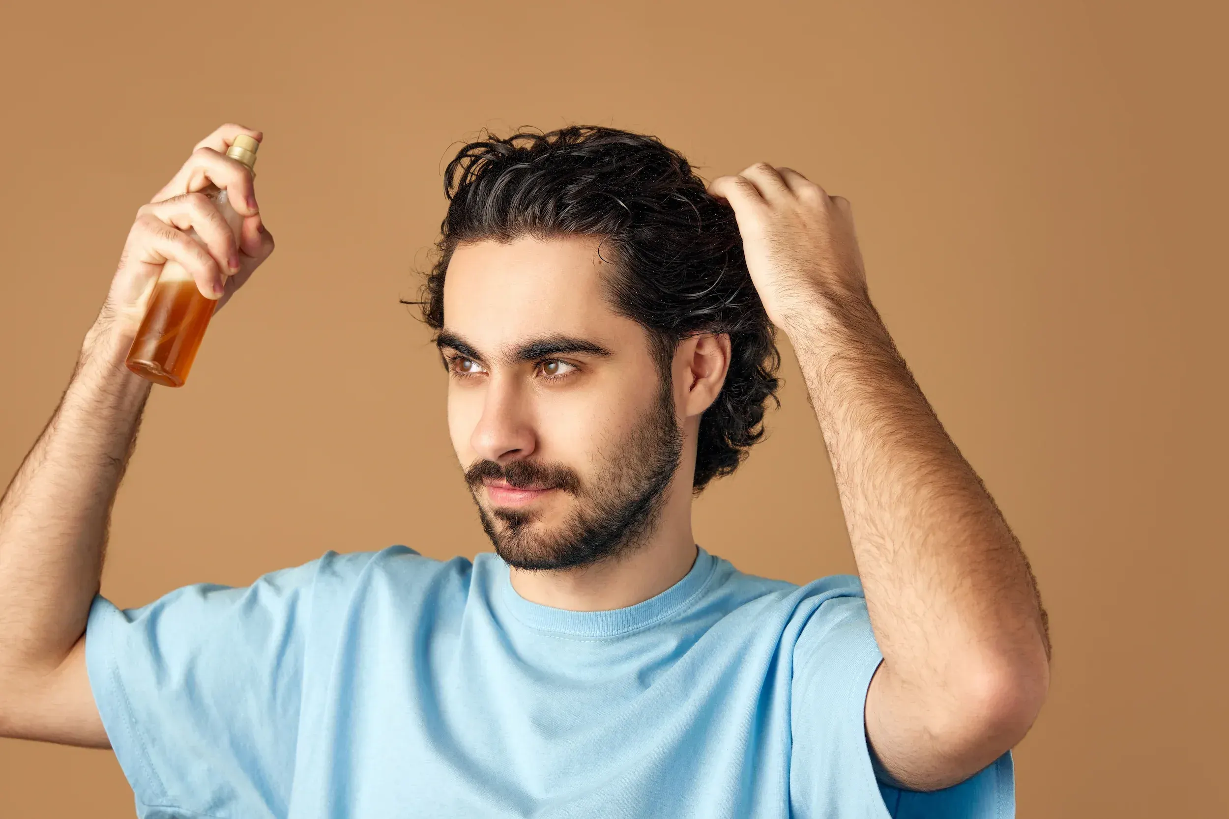 Man applying hair treatment spray to dark curly hair - hair restoration products at ANU Face Mind Body Elizabethtown KY