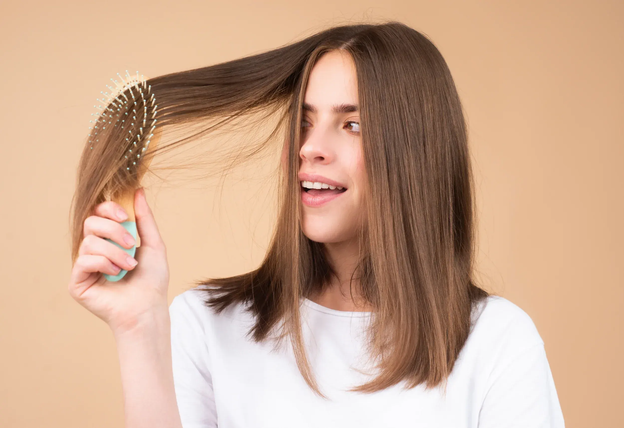 Young woman brushing healthy brown hair and smiling - hair loss and thinning treatment at ANU Face Mind Body Elizabethtown KY