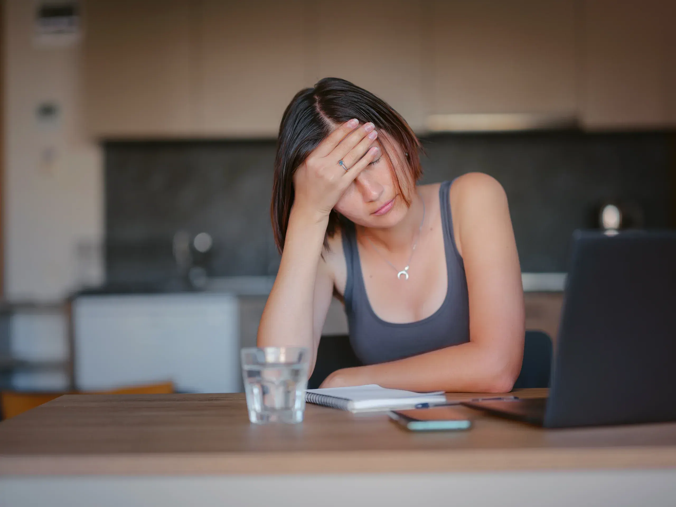 Woman resting head in hand at kitchen table looking stressed and overwhelmed - anxiety and depression treatment at ANU Face Mind Body Elizabethtown KY