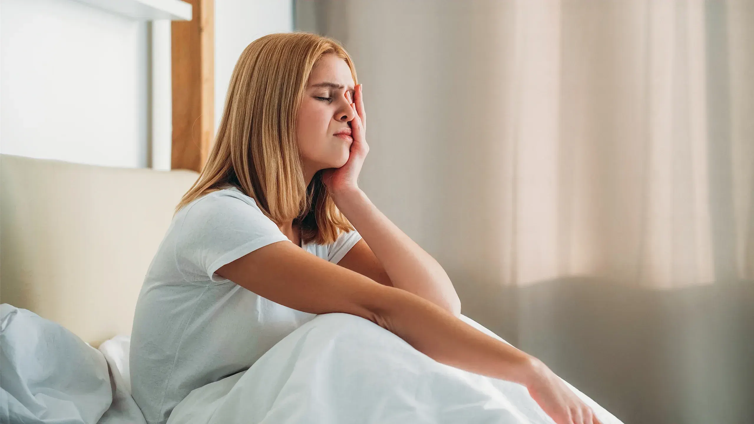 Woman sitting on bed looking fatigued and emotionally drained - recognizing symptoms of anxiety and depression