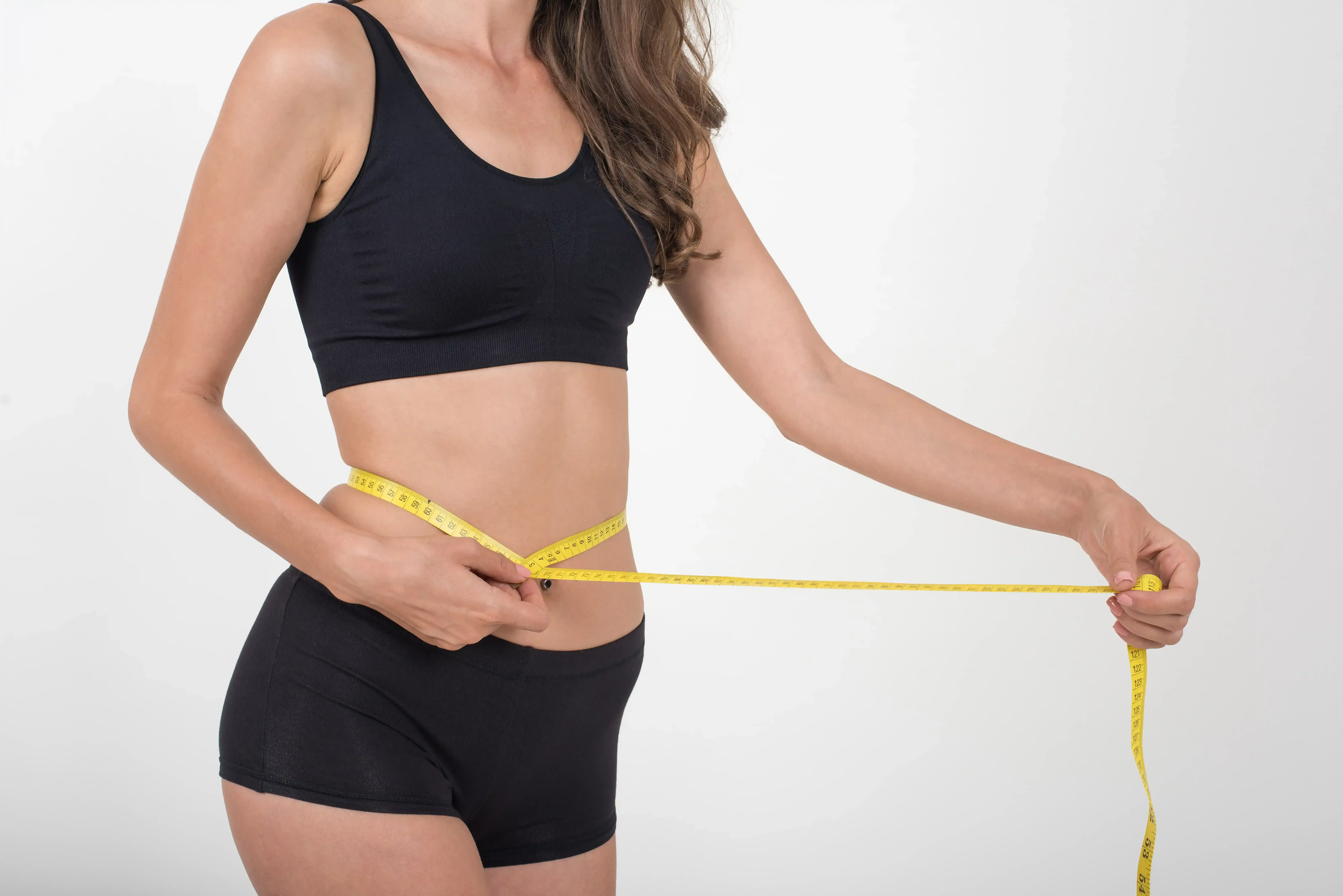 Fit woman in athletic wear measuring slim waistline with tape measure - weight management results at ANU Face Mind Body
